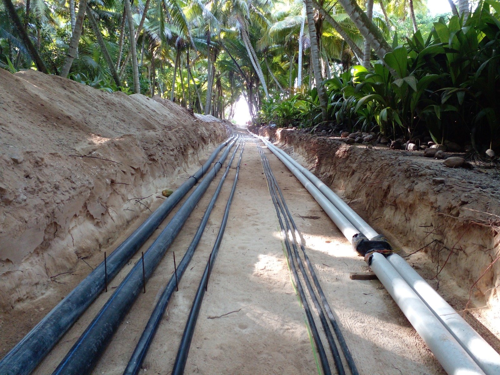 External services trench with HDPE mains, direct-buried LV cabling and uPVC ducts on a sand bed