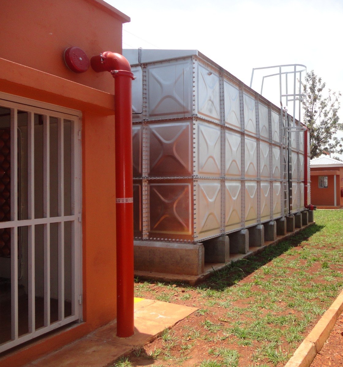 Sectional GRP fire water storage tank on precast plinths, with the fire main riser and alarm gong at the pump house