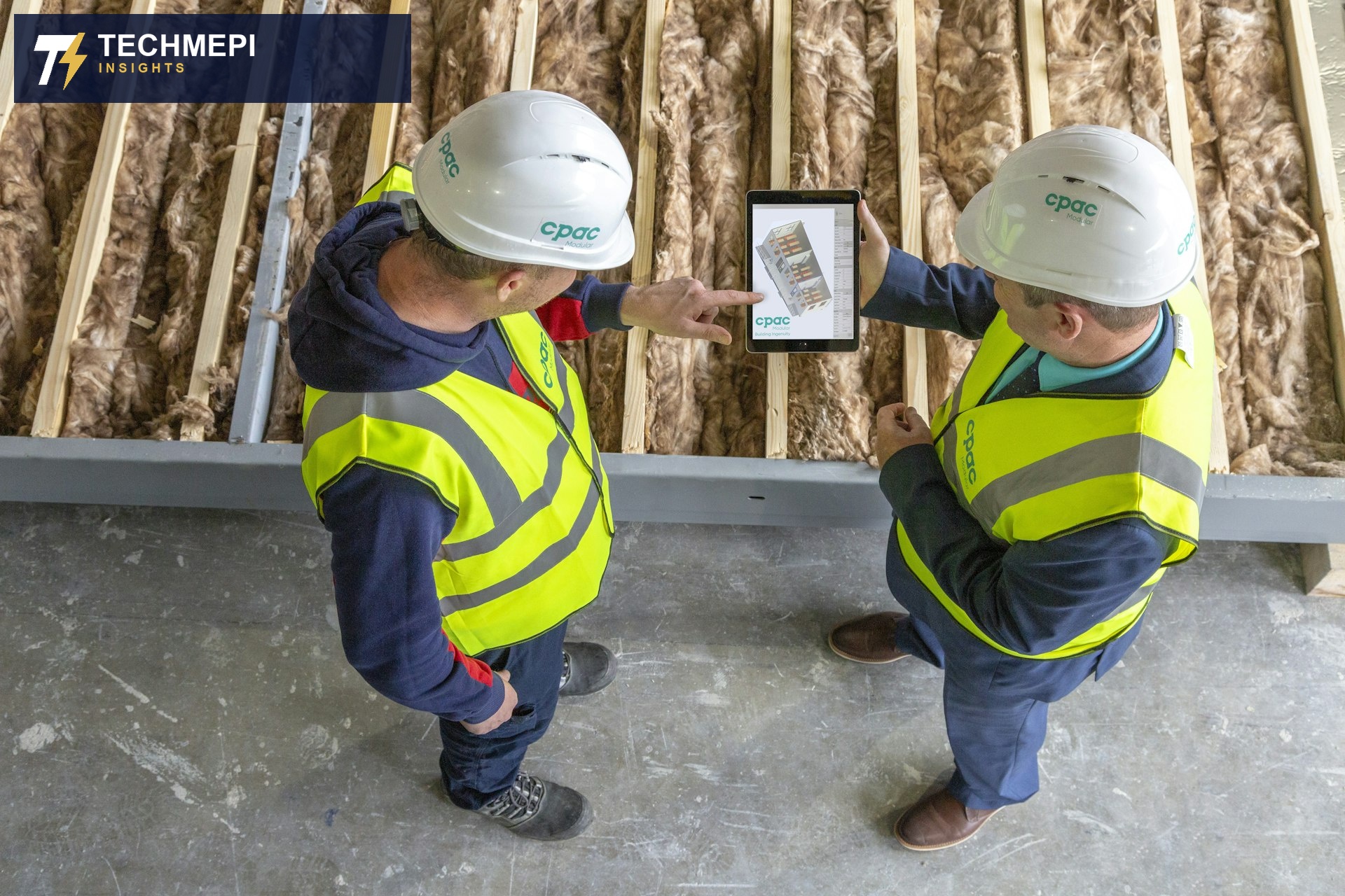 Two engineers in hard hats and hi-vis vests reviewing a 3D BIM model on a tablet at a construction site